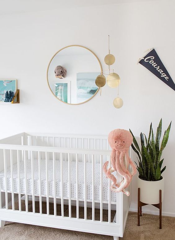 an ocean-inspired nursery with a statement plant, white furniture, polka dots and a pink octopus