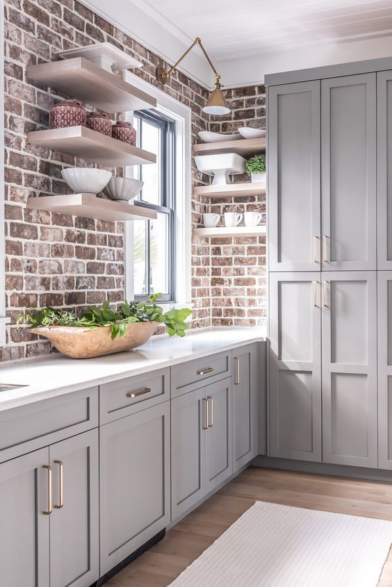 An Elegant Grey Farmhouse Kitchen with Vintage-Inspired Cabinets, Brick Walls, and a White Stone Countertop