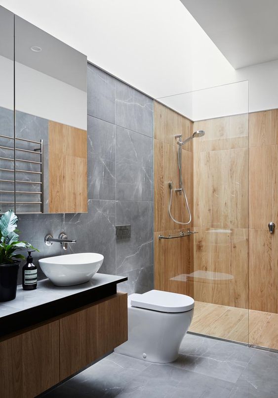 a contemporary bathroom with grey marble tiles and wooden paneling in the shower space, a floating vanity and a skylight