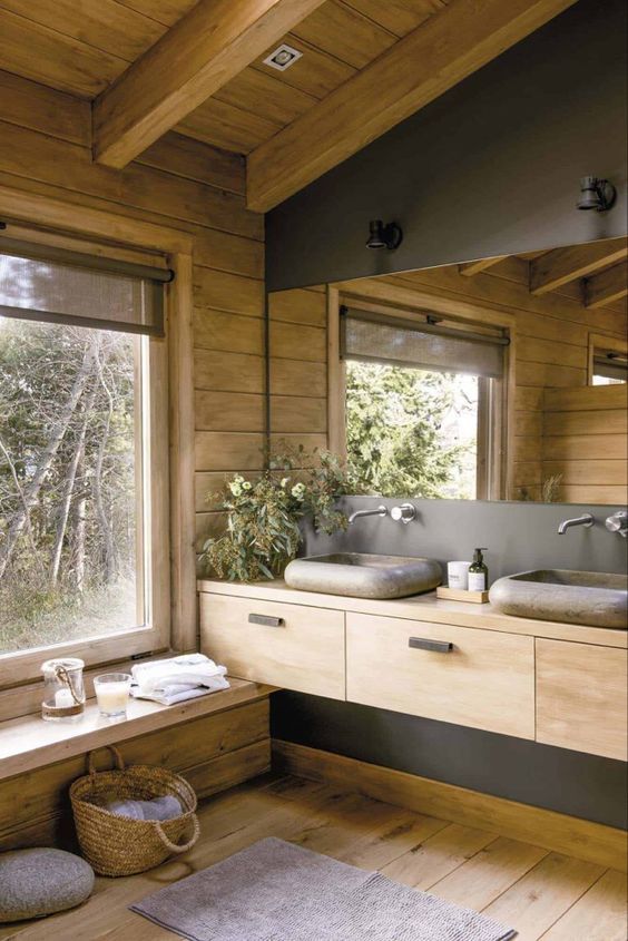 a cabin bathroom of wood and concrete, with stone sinks, a large mirror and a large window for a view