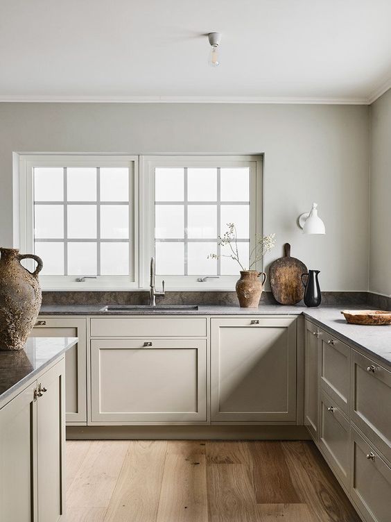 a warm and welcoming greige Scandinavian kitchen with vintage cabients and walls matching in color, dark countertops and a tiny backsplash