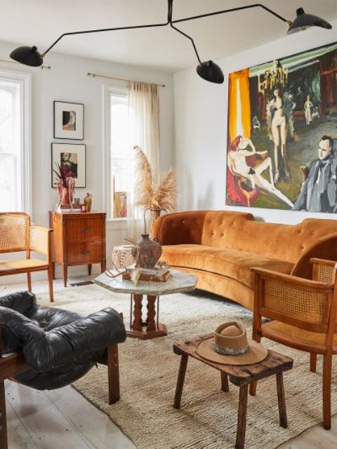 a modern and boho living room with a rust-colored sofa, rattan chairs, wooden and leather furniture and a statement artwork