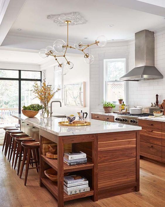 a welcoming mid-century modern walnut kitchen with stylish cabinets and a large kitchen island, white stone countertops and a catchy chandelier