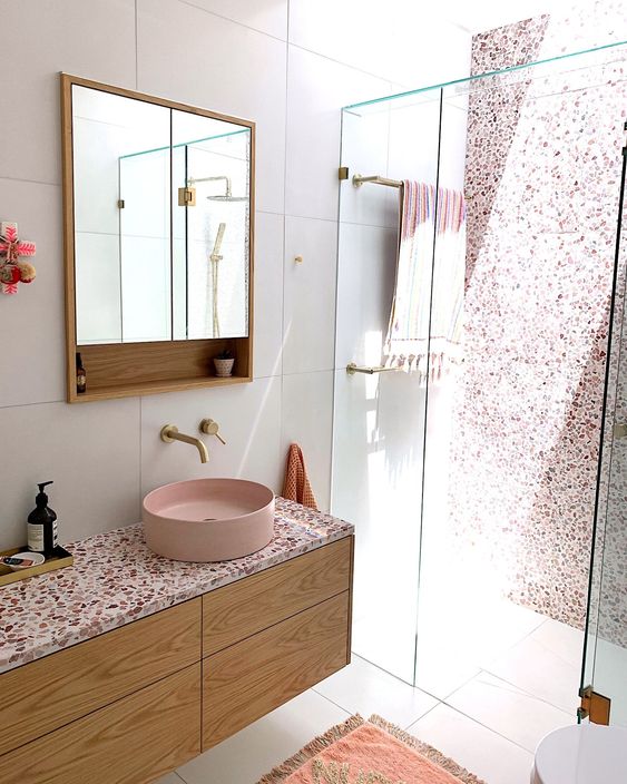 a chic contemporary bathroom with a pink terrazzo wall in the shower, a floating vanity with a pink terrazzo countertop plus a pink sink