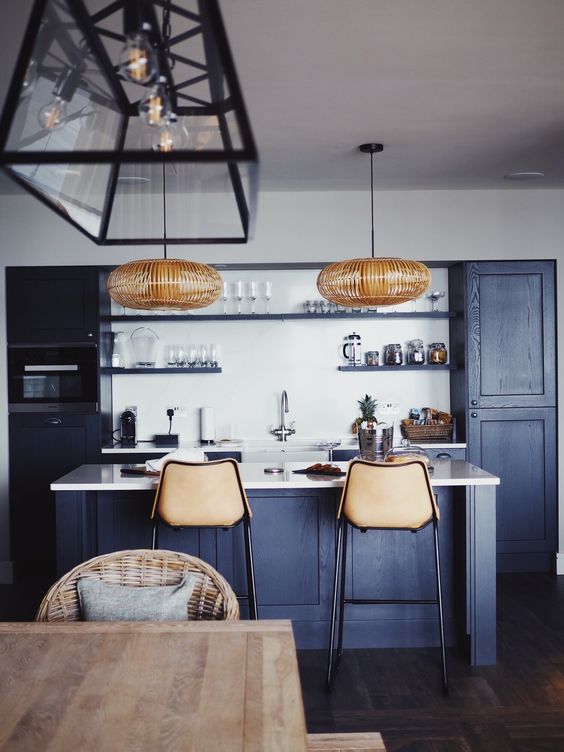 a cool contemporary navy kitchen with white countertops and a backsplash, rattan lamps and leather stools