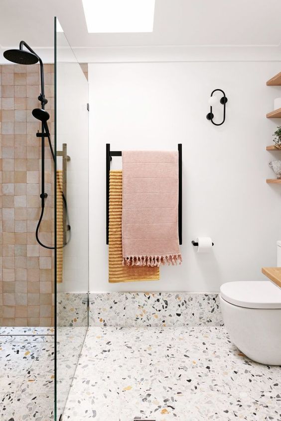 a contemporary bathroom with white tiles, a terrazzo floor, pink tiles, black fixtures and a skylight