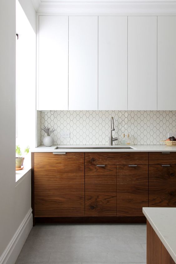 a two tone kitchen with sleek white cabinets and rich toned walnut ones, a white geo tile backsplash and white countertops