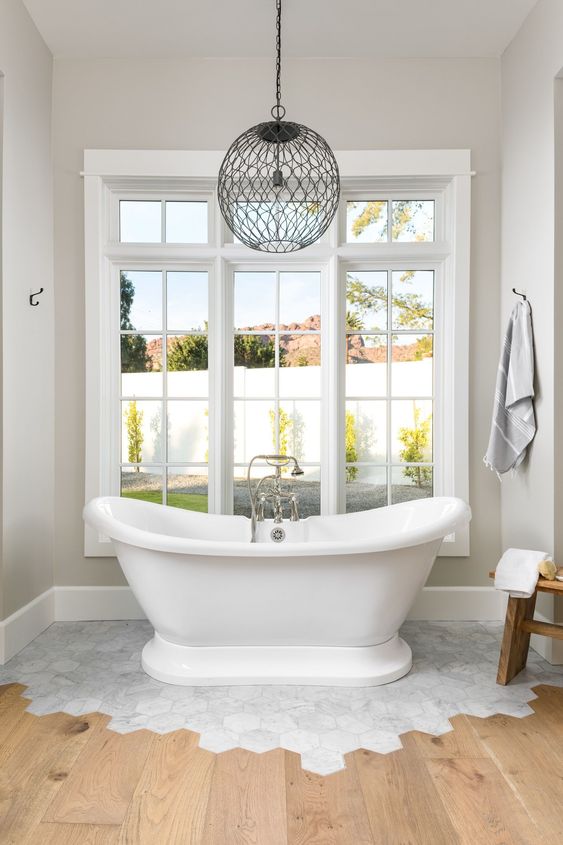 a vintage bathroom with neutral walls, a white marble hex tile floor and wooden floors plus a vintage bathtub and a pendant lamp