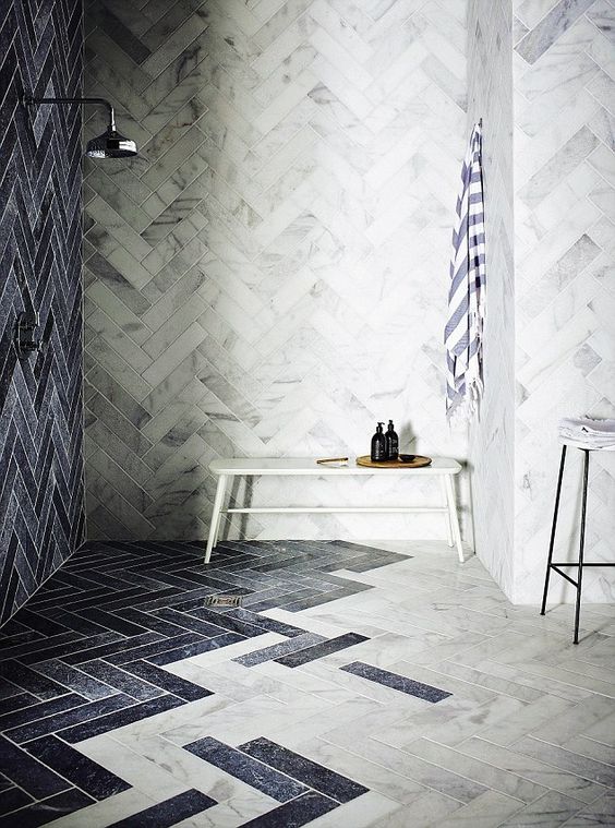 a chic bathroom with white marble tiles and navy ones, with a bench, a stool and neutral fixtures