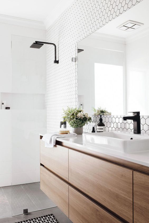 a contemporary bathroom with white hex tiles, a sleek wooden vanity, black fixtures and a large mirror