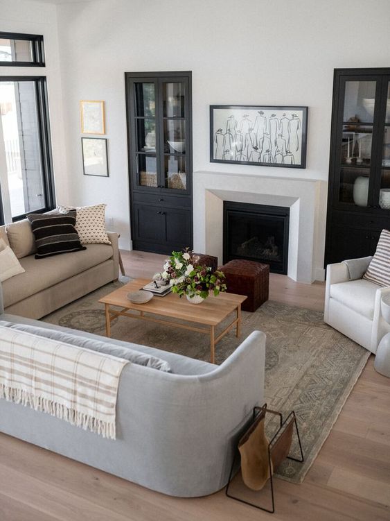 a chic neutral living room with a fireplace, neutral and pastel curved furniture, a wooden table and built-in storage units