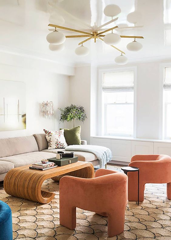 a neutral living room spruced up with bright furniture and decor, with orange curved chairs and a creative curved coffee table