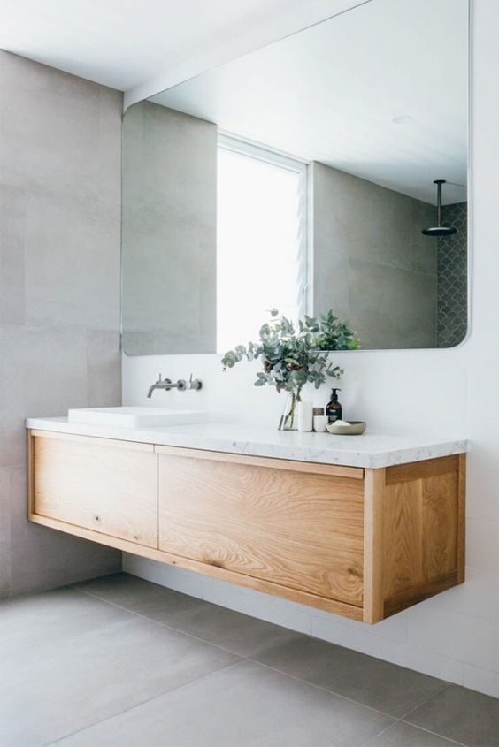 a contemporary bathroom with a wood and stone floating vanity, a large mirror and large scale grey tiles