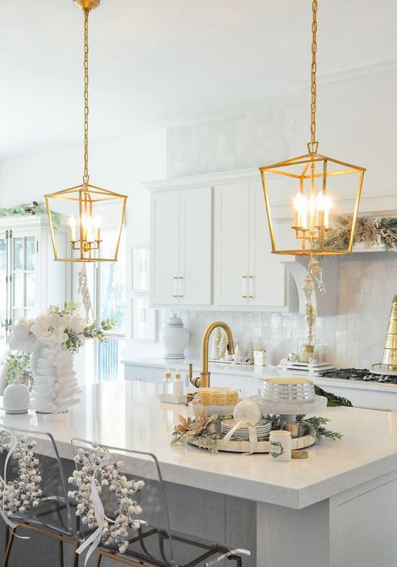 a neutral kitchen with a white tile backsplash and white countertops, gold pendant lamps and gold fixtures