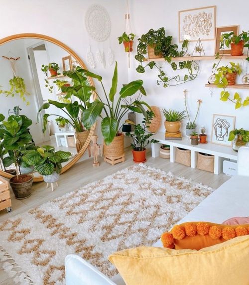 a light-filled boho living room in neutrals, with potted plants, a large round mirror and bright textiles