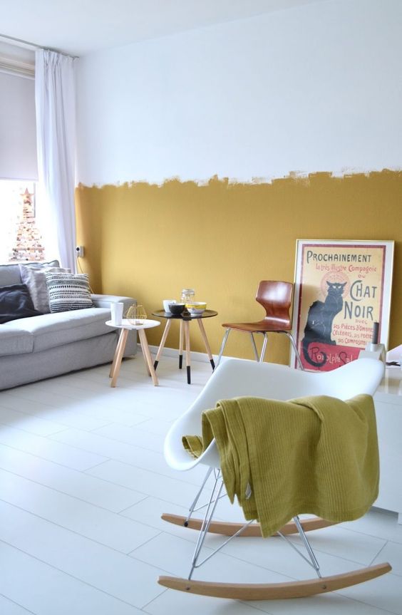 a contemporary living room with a mustard color block wall, chic furniture, round tables and a rocker and a vintage poster