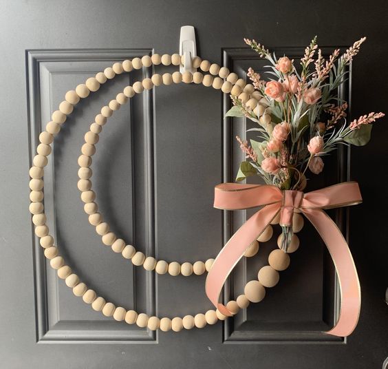 a modern boho wreath of wooden beads, with greenery, blush blooms and a pink ribbon bow is a lovely and cool idea