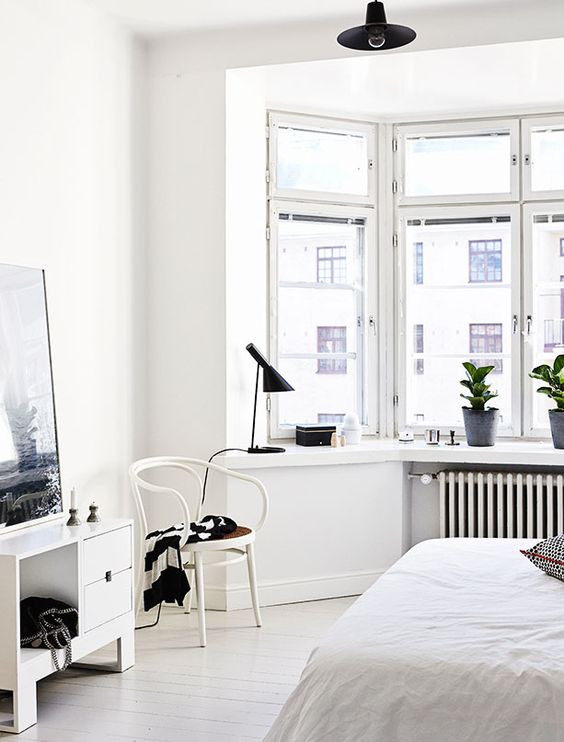 a Nordic bedroom in white, with a bow window and much light, plus touches of black for more drama