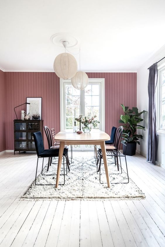 a Scandinavian dining room with a mauve wall, a wooden table, mismatching chairs, paper lamps and a dark buffet