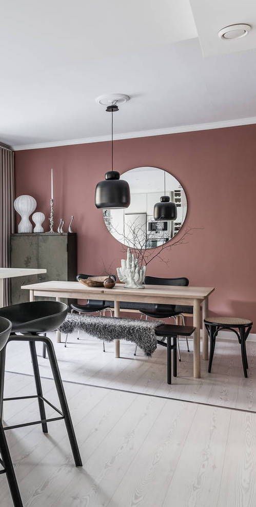 a Scandinavian dining room with mauve walls, chic furniture, an olive green buffet, black touches and a round mirror