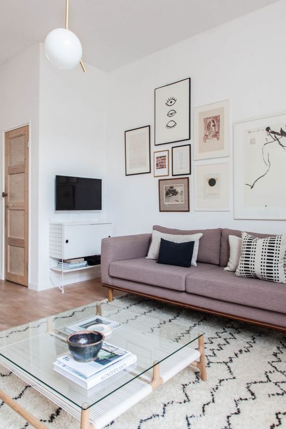 a Scandinavian living room in neutrals, with a mauve sofa, a monochromatic gallery wall and a cool coffee table