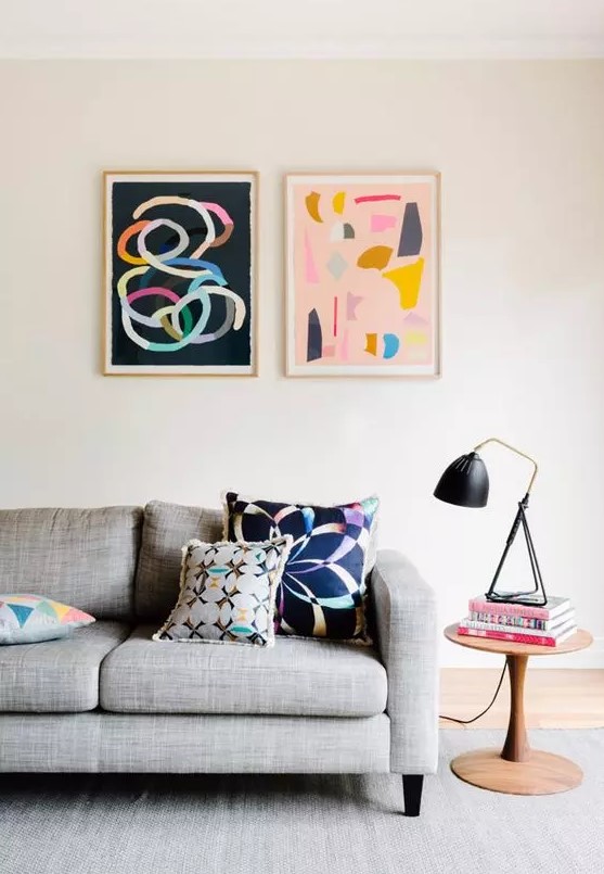 a Scandinavian living room with a grey sofa, a rug, a side table and colorful artwork to add a bit of fun to the space