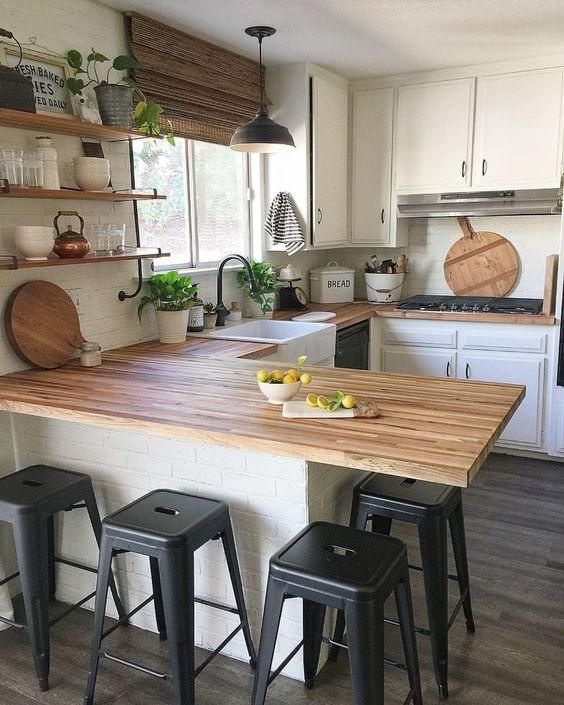 a U-shaped kitchen with white cabinetry, butcherblock countertops and a woven shade plus black stools