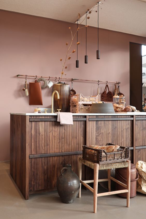 a beautiful mauve kitchen with a large wood clad kitchen island, pendant lamps, stools and various vases and buckets
