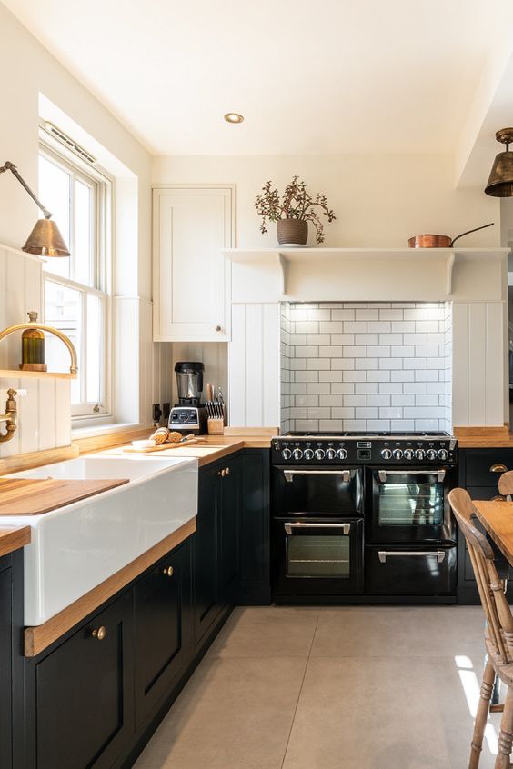 a black L-shaped farmhouse kitchen with butcherblock countertops, a white tile backsplash and pretty vintage lamps is cool