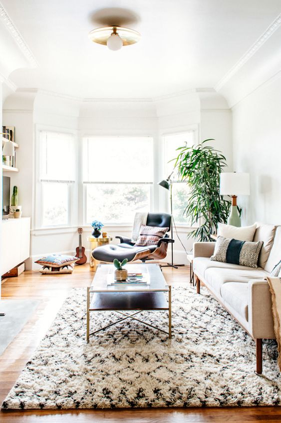 a boho lux living room with a bow window, a comfy lounger next to it, a neutral sofa and a low coffee table plus potted plants