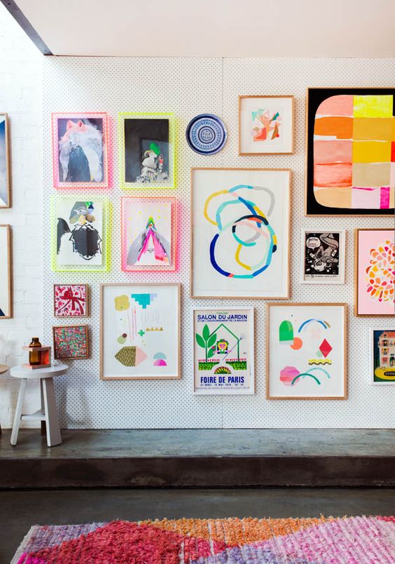 a bright gallery wall with abstract artworks and prints, with neon ligth frames and usual ones for a funky look