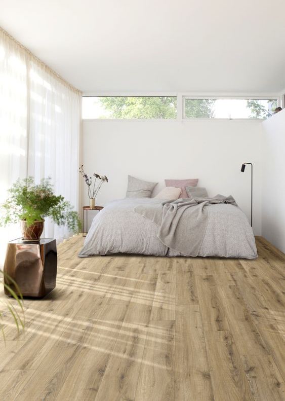 a chic minimalist bedroom with white walls, a glazed wall and clerestory windows, a bed with grey bedding and some plants