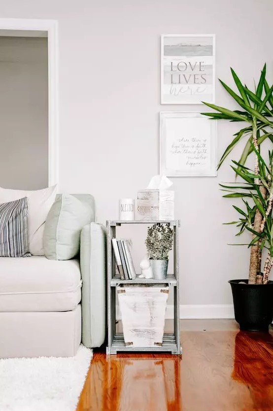 a chic neutral living room with a green and creamy sofa and pillows, a side table, a mini gallery wall and a potted plant