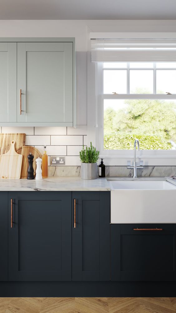 a chic two tone kitchen with light green and graphite grey shaker cabinets, a white subway tile backsplash and white marble countertops