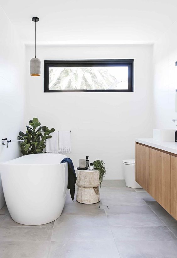 a contemporary bathroom with a floating vanity, an oval tub, a pendant lamp and a clerestory window plus some greenery