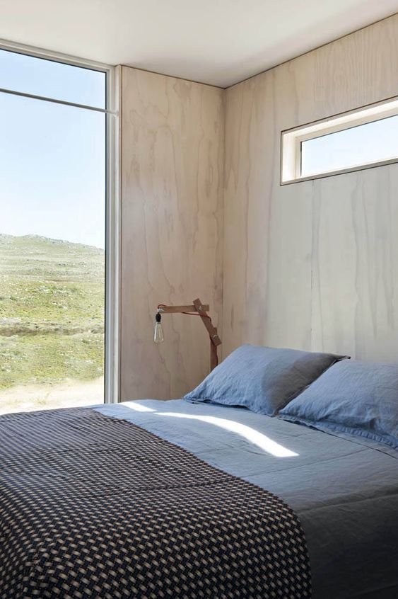 a contemporary bedroom with blonde wood walls, a comfy bed, a glazed wall and a clerestory window for additional light