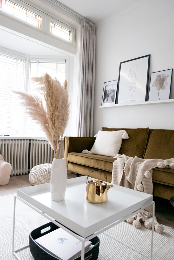 a contemporary living room with a bow window and a seating zone there, a green sofa, a pretty table and a ledge gallery wall