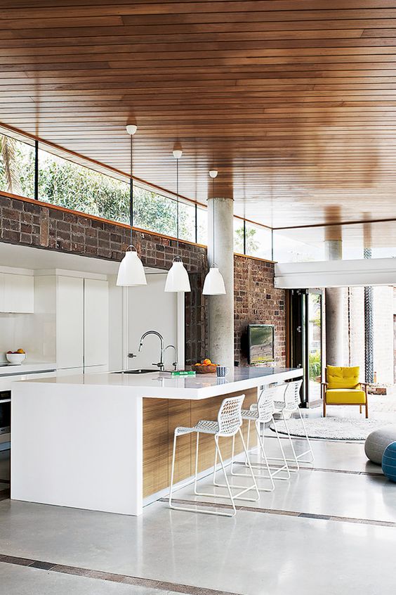 a contemporary space with a brick wall, white sleek cabinetry, pendant lamps and clerestory windows that birng light in