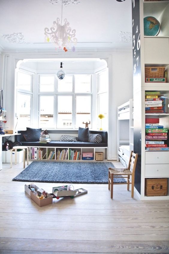 a cool kids' room with a bunk bed, a bow window with a windowsill sofa and built-in bookshelves plus a cool chandelier