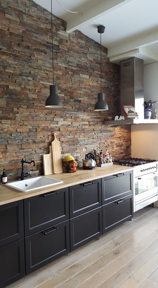 a cozy black one wall kitchen with butcherblock countertops and a faux stone wall plus pendant lamps is chic