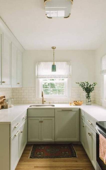 a cozy light green farmhouse kitchen with white stone countertops and a white tile backsplash plus a vintage lamp