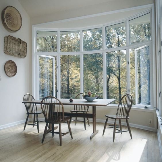 a farmhouse dining zone by a large bow window, with a vintage table and chairs plus decorative baskets on the wall