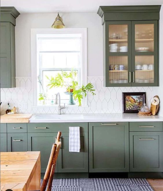 a green one wall kitchen with a pretty white tile backsplash, a white countertop and brass touches plus a printed rug