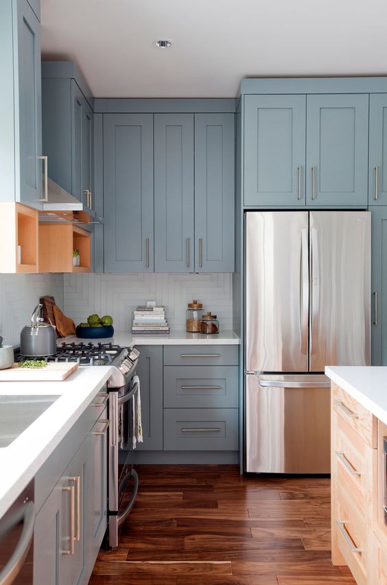 a light blue shaker style kitchen with a white square tile backsplash, white countertops and stainless steel handles is super chic and airy