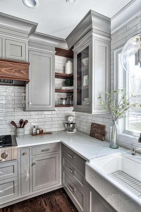 a light grey kitchen with shaker cabinets, white countertops, a white skinny tile backsplash and touches of stained wood