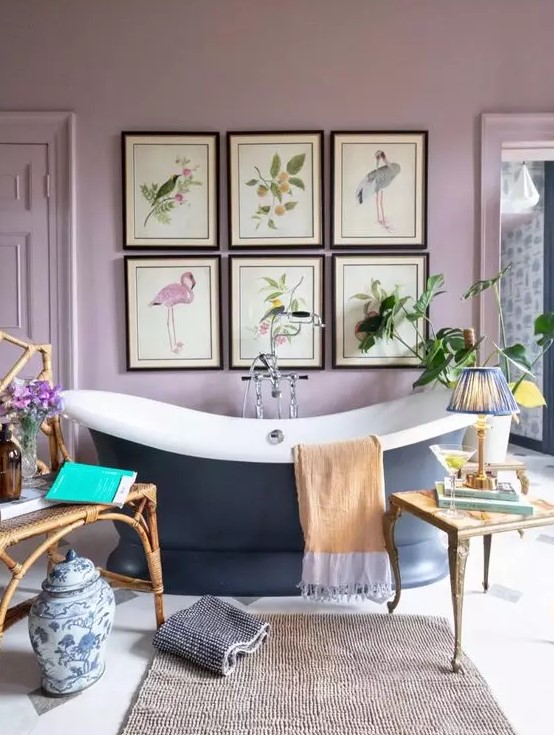 a lilac vintage bathroom with a chic gallery wall, a navy oval tub, a rug and some lovely coffee tables plus potted greenery
