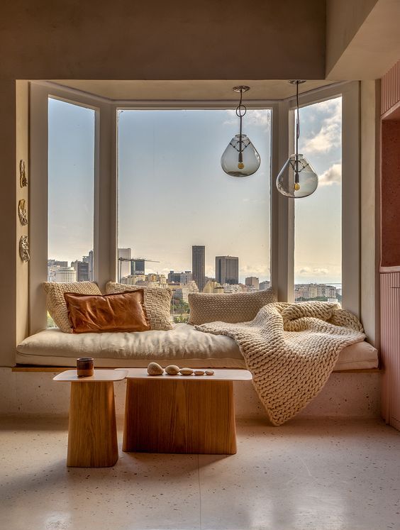a lovely bow window with a windowsill daybed and pillows, pendant lamps over the bed and a duo of tables