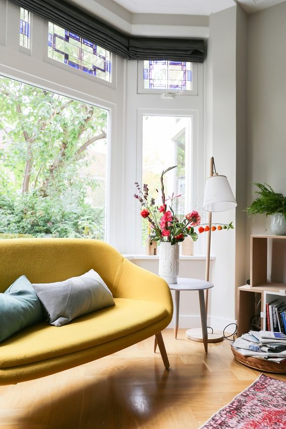 a lovely nook with a bow window with mosaic glass and a yellow loveseat plus a bookshelf next to it is cozy