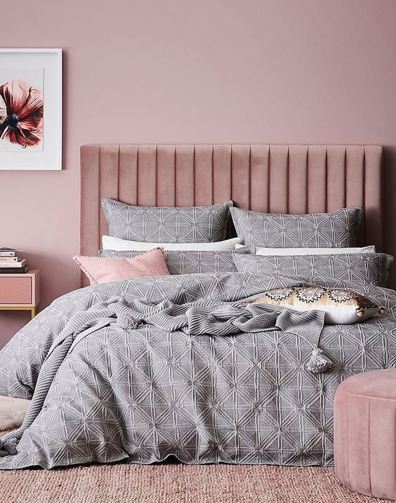 a mauve bedroom with a pink upholstered bed and ottoman, pink nightstands and pretty grey and pink bedding