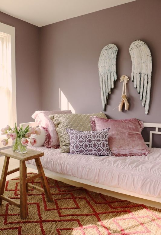 a mauve bedroom with a single bed, a stool and pink bedding plus creative art on the wall